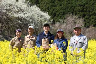 お米を抱え、満開の菜の花に囲まれる池田農園さんの写真