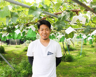 ぶどう棚の下で笑顔の丸山農園さんの写真