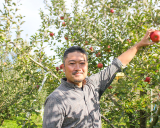 りんごに手をかけて、笑顔の松葉園さんの写真