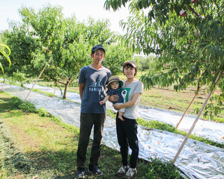 果樹園で子どもを抱くまつじるし農園さんの写真
